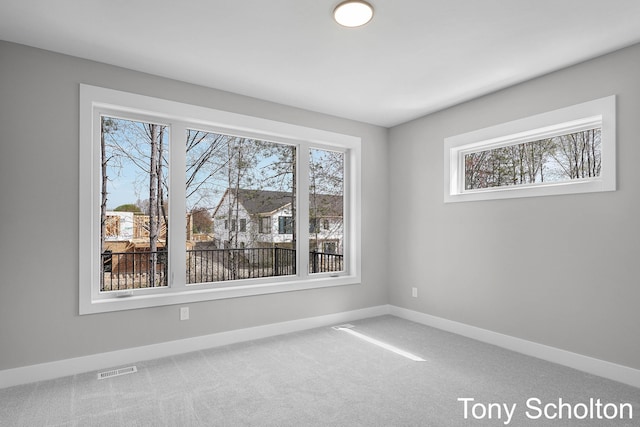 carpeted spare room with baseboards, a wealth of natural light, and visible vents