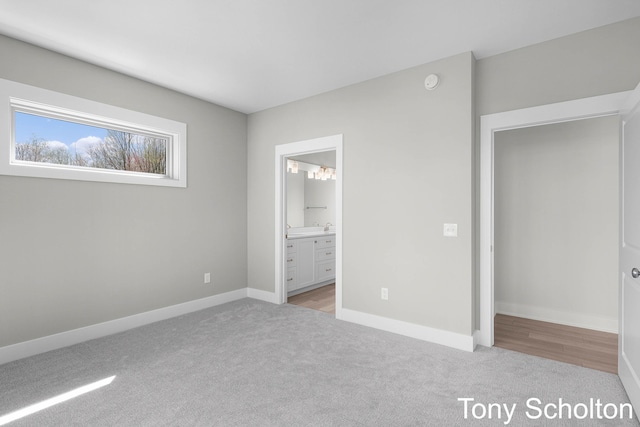 unfurnished bedroom featuring baseboards, ensuite bathroom, and light carpet