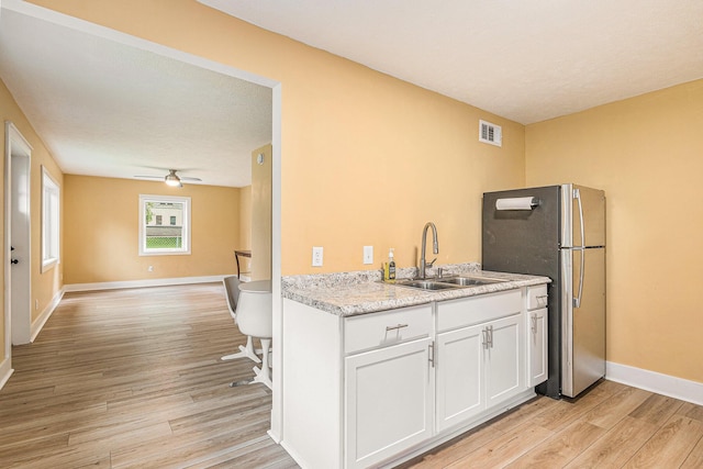 kitchen featuring white cabinetry, light hardwood / wood-style floors, sink, stainless steel fridge, and ceiling fan