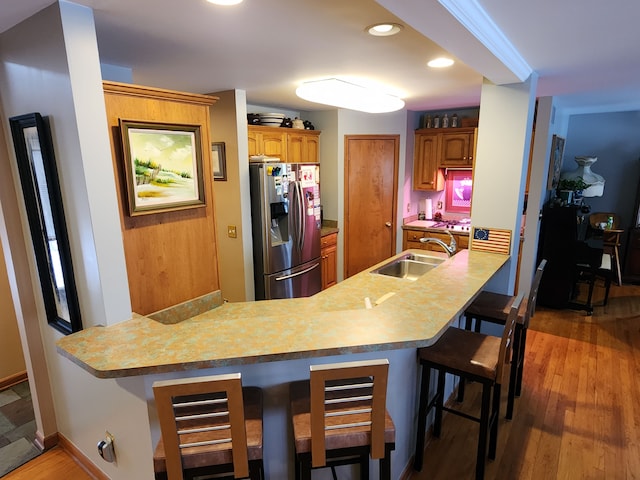 kitchen featuring kitchen peninsula, sink, light wood-type flooring, stainless steel fridge with ice dispenser, and a breakfast bar area