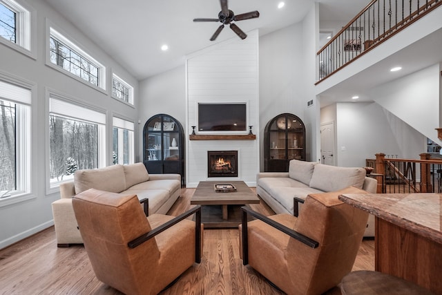 living room with high vaulted ceiling, ceiling fan, a fireplace, and light hardwood / wood-style flooring