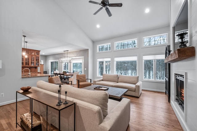 living room featuring high vaulted ceiling, light hardwood / wood-style floors, sink, and ceiling fan with notable chandelier