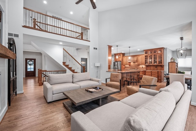 living room featuring ceiling fan, light hardwood / wood-style flooring, and a towering ceiling