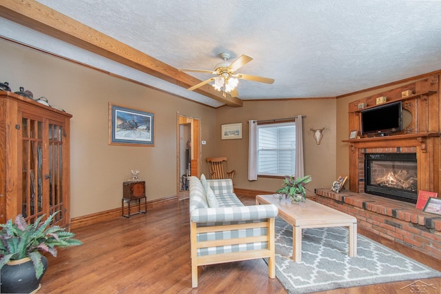 living room featuring hardwood / wood-style floors, a brick fireplace, ceiling fan, a textured ceiling, and ornamental molding