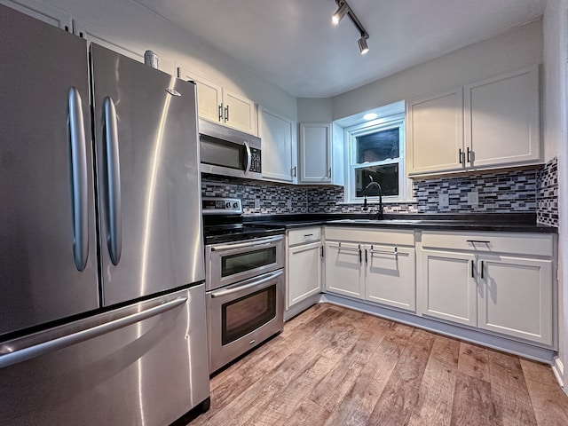 kitchen featuring white cabinets, appliances with stainless steel finishes, decorative backsplash, sink, and light wood-type flooring