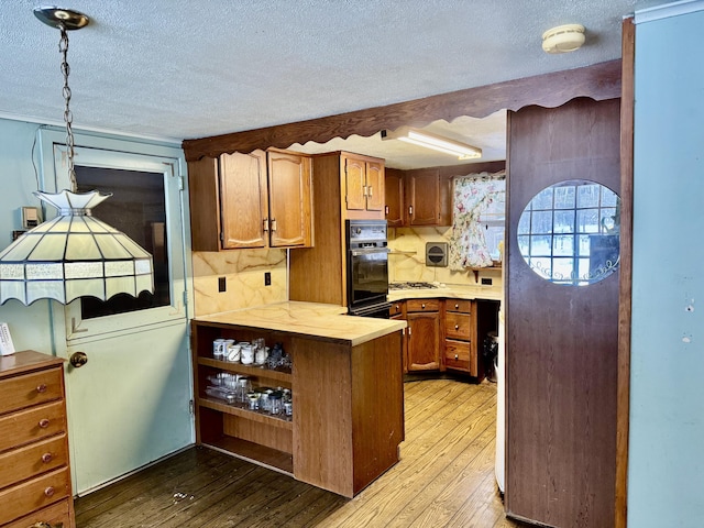 kitchen with a textured ceiling, black oven, and light hardwood / wood-style flooring