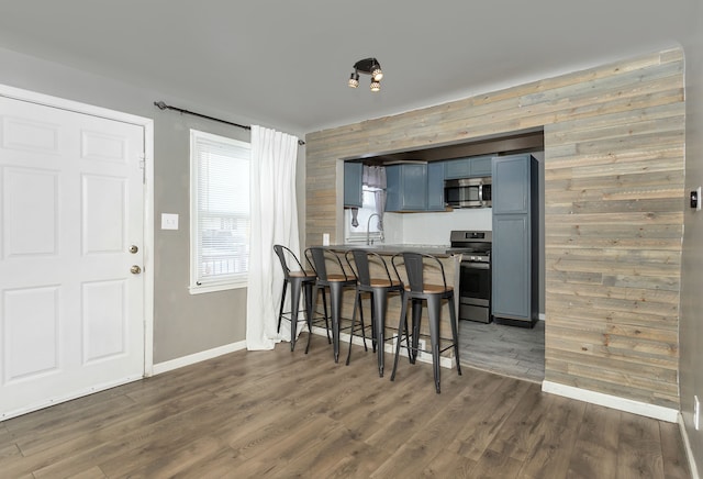 kitchen with wood walls, kitchen peninsula, appliances with stainless steel finishes, a kitchen breakfast bar, and dark hardwood / wood-style flooring