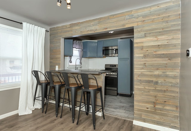 kitchen with kitchen peninsula, appliances with stainless steel finishes, dark wood-type flooring, blue cabinets, and a breakfast bar