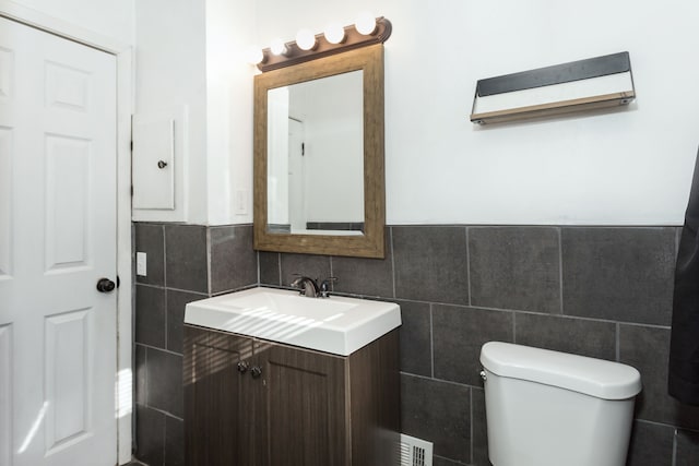 bathroom with toilet, vanity, and tile walls