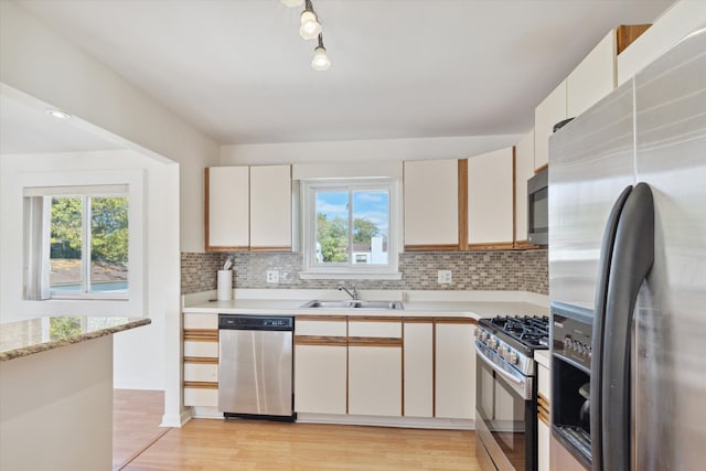 kitchen featuring backsplash, light hardwood / wood-style floors, sink, white cabinetry, and stainless steel appliances