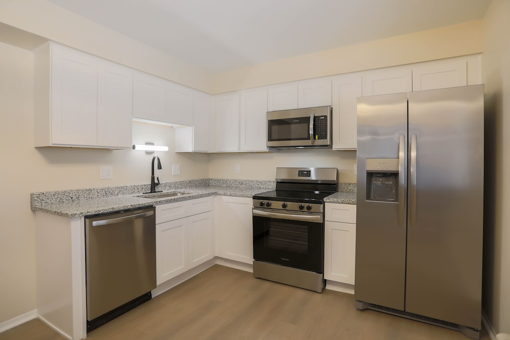 kitchen with light stone countertops, white cabinetry, stainless steel appliances, sink, and light hardwood / wood-style flooring