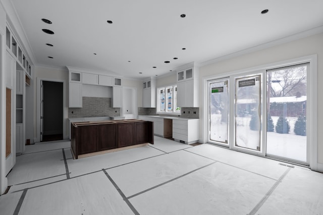 kitchen with decorative backsplash, dark brown cabinets, ornamental molding, white cabinets, and a center island