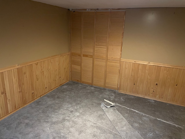 unfurnished bedroom with a closet, wooden walls, and dark colored carpet