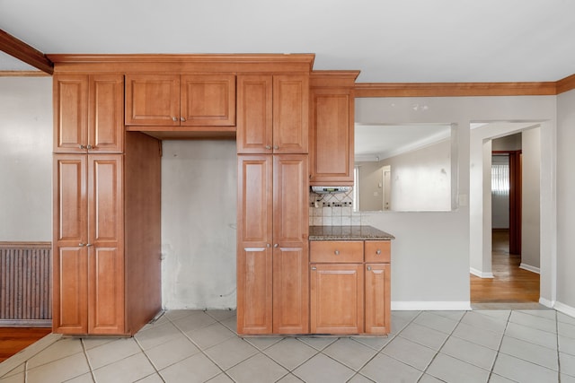 kitchen featuring light tile patterned floors, crown molding, dark stone counters, and decorative backsplash