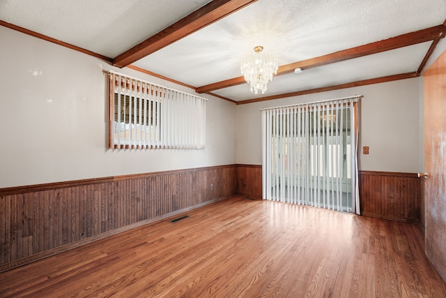 empty room with beam ceiling, wooden walls, a notable chandelier, a textured ceiling, and light wood-type flooring