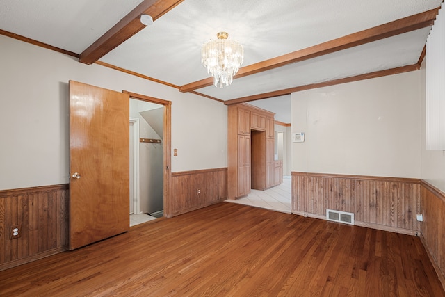 empty room with a chandelier, light hardwood / wood-style flooring, ornamental molding, wooden walls, and beam ceiling