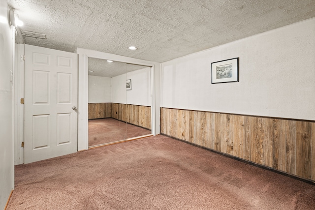 carpeted spare room with wooden walls and a textured ceiling