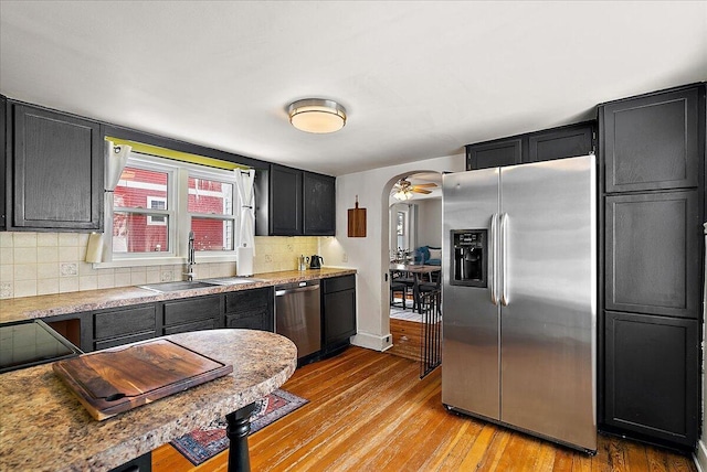 kitchen with ceiling fan, stainless steel appliances, decorative backsplash, light wood-type flooring, and sink