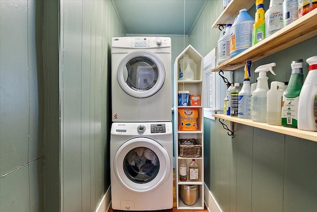 laundry area with stacked washer / dryer, crown molding, and wooden walls