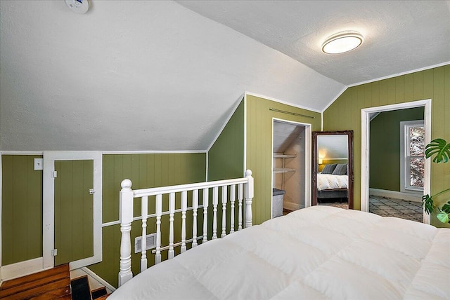 bedroom featuring a textured ceiling, wooden walls, and vaulted ceiling