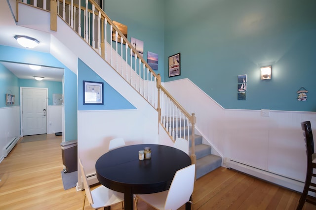 dining space with baseboard heating, a towering ceiling, and wood-type flooring