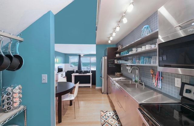 kitchen featuring stainless steel counters, backsplash, sink, light wood-type flooring, and stainless steel appliances