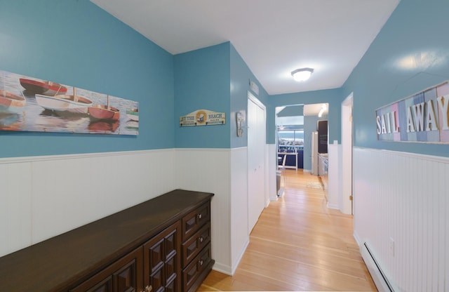 corridor with light wood-type flooring and a baseboard heating unit