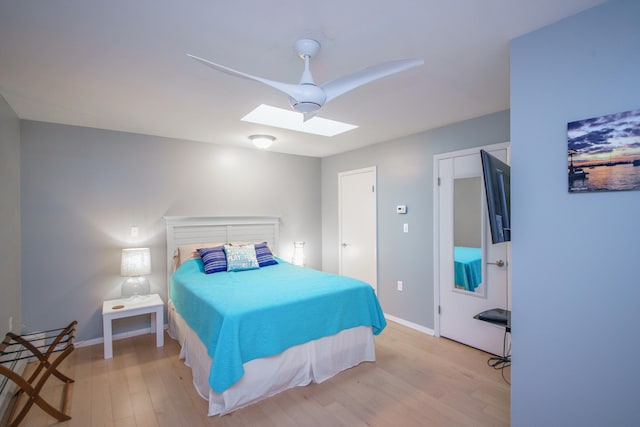 bedroom with ceiling fan, a skylight, and light hardwood / wood-style floors