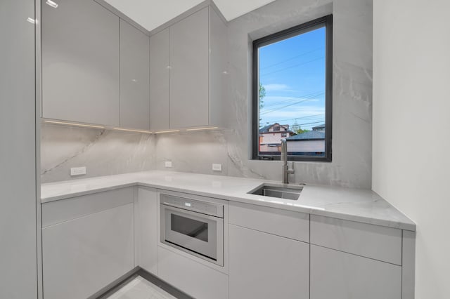 kitchen featuring decorative backsplash, light stone countertops, sink, and wall oven