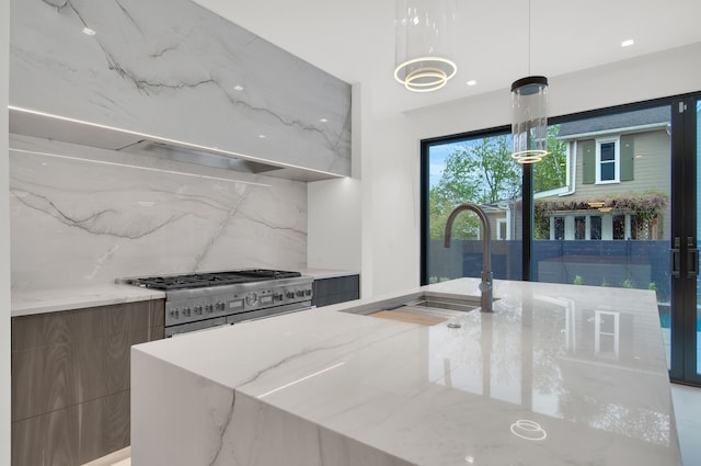 kitchen with backsplash, double oven range, sink, hanging light fixtures, and light stone counters