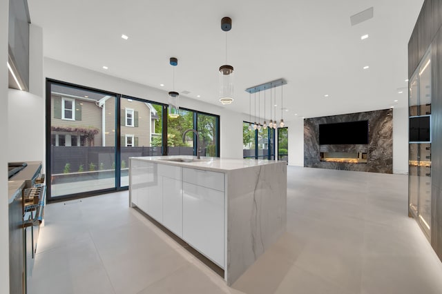 kitchen featuring sink, hanging light fixtures, a kitchen island with sink, white cabinets, and light stone counters