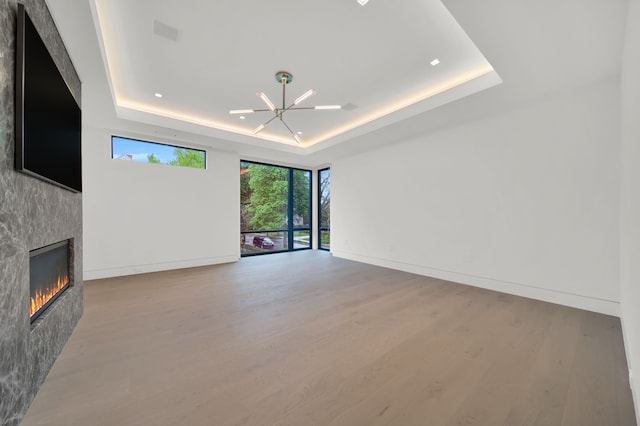 unfurnished living room with a large fireplace, a tray ceiling, a chandelier, and light hardwood / wood-style flooring