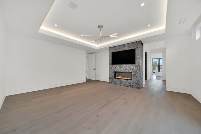 unfurnished living room featuring a raised ceiling, ceiling fan, a fireplace, and hardwood / wood-style flooring