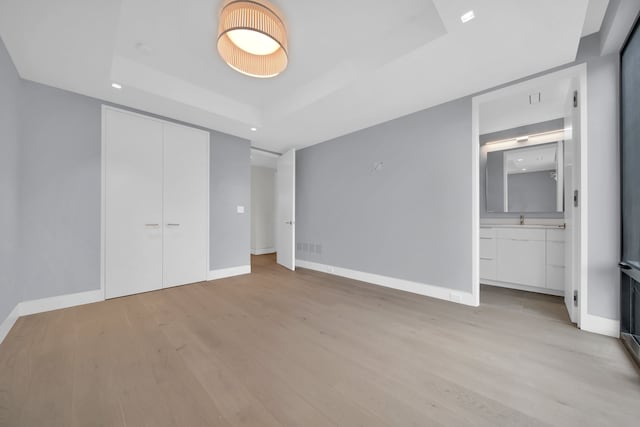 unfurnished bedroom with a closet, light hardwood / wood-style flooring, and a tray ceiling