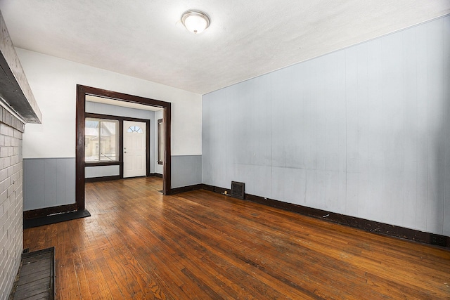 spare room with a brick fireplace and dark hardwood / wood-style flooring