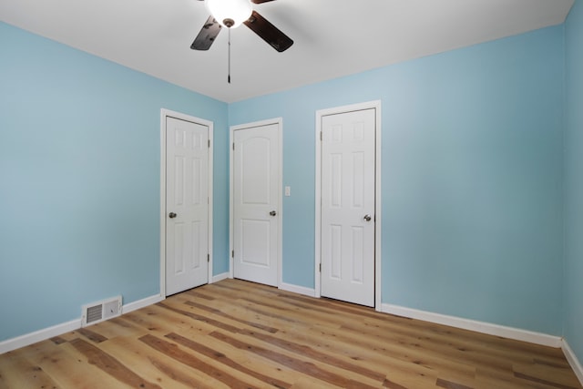 unfurnished bedroom with ceiling fan, two closets, and light wood-type flooring