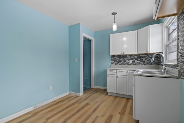 kitchen featuring decorative light fixtures, white cabinetry, light hardwood / wood-style floors, decorative backsplash, and sink