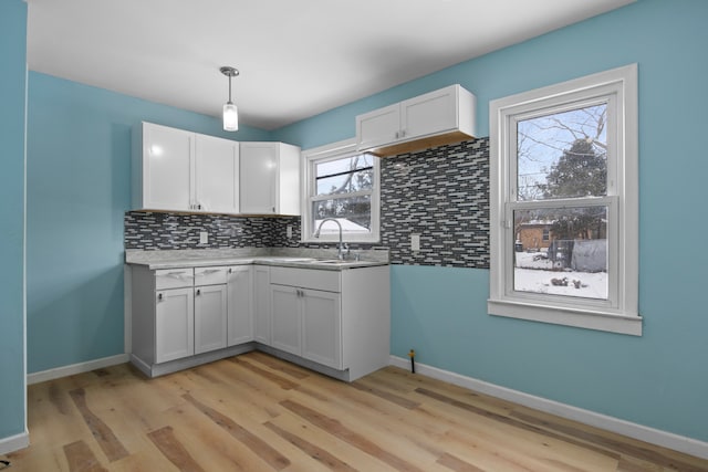 kitchen featuring backsplash, light wood-type flooring, hanging light fixtures, white cabinets, and sink