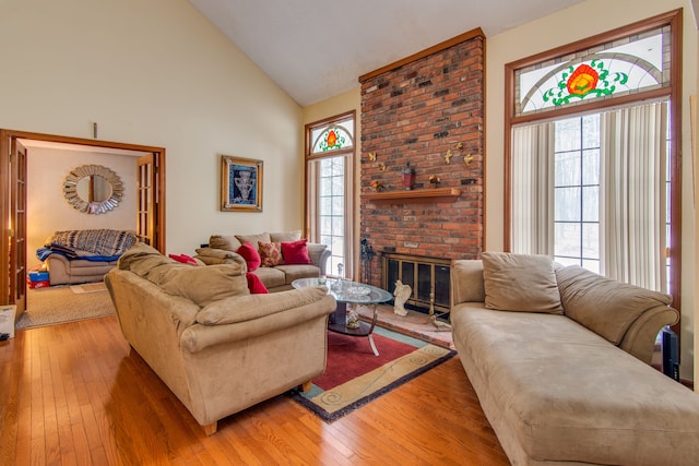 living room with a brick fireplace, light hardwood / wood-style flooring, and high vaulted ceiling