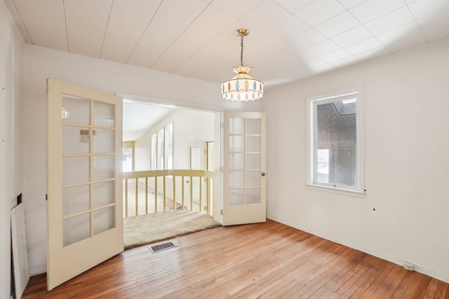 empty room with light wood-type flooring, plenty of natural light, a chandelier, and french doors