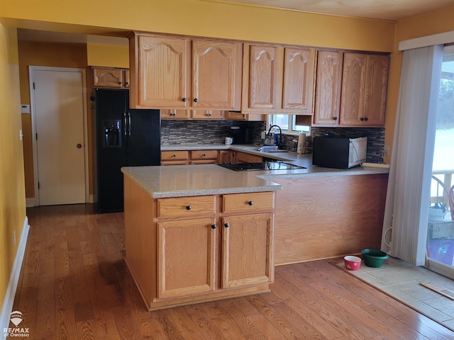 kitchen with kitchen peninsula, backsplash, black fridge, light hardwood / wood-style flooring, and sink