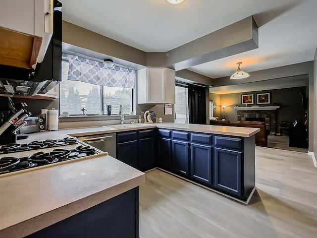 kitchen featuring kitchen peninsula, light wood-type flooring, pendant lighting, white cabinets, and sink