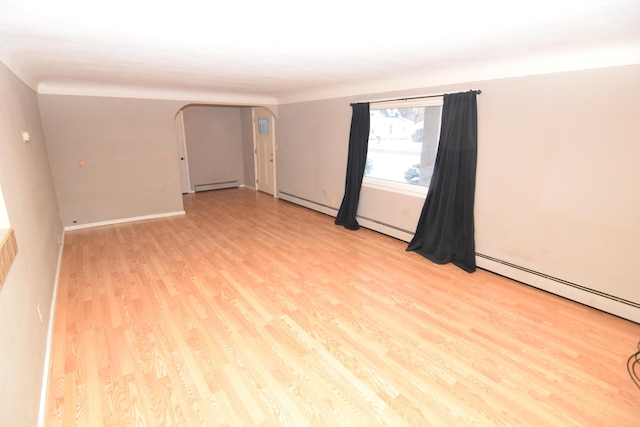 spare room featuring baseboard heating and light hardwood / wood-style floors