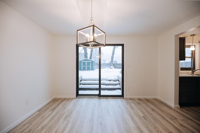 unfurnished dining area with sink, a chandelier, and light hardwood / wood-style floors