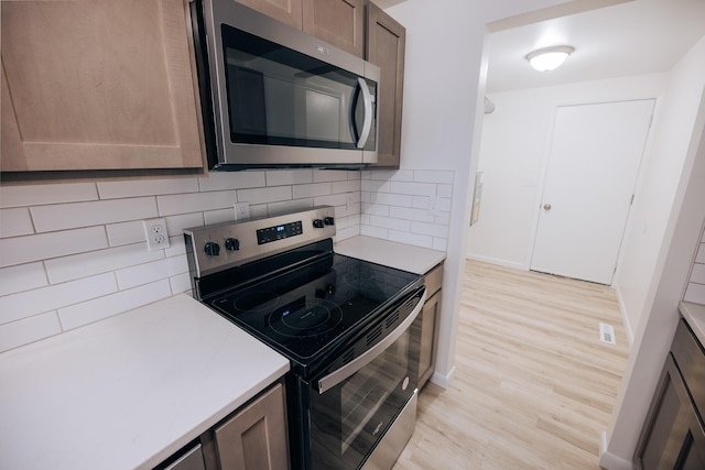 kitchen with light wood-type flooring, stainless steel appliances, and backsplash