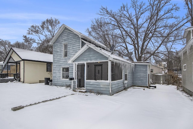 snow covered rear of property featuring a sunroom