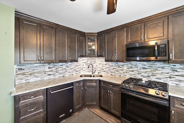 kitchen featuring stainless steel appliances, backsplash, light stone counters, dark brown cabinetry, and sink