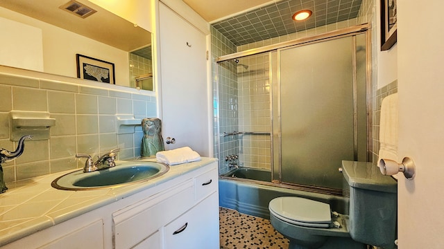 full bathroom with toilet, bath / shower combo with glass door, tile walls, vanity, and decorative backsplash