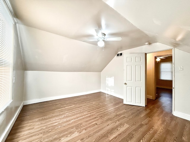 additional living space with vaulted ceiling, ceiling fan, a healthy amount of sunlight, and wood-type flooring