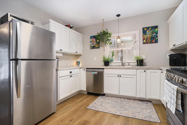 kitchen with decorative light fixtures, light hardwood / wood-style floors, sink, white cabinetry, and stainless steel appliances